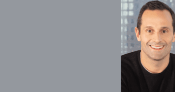 Professional portrait of a smiling man with a blurred city background, suitable for a corporate profile or business banner