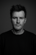 Black-and-white portrait of Brad Reilly, Chief Creative Officer at VIRTUE, looking directly at the camera against a dark background.