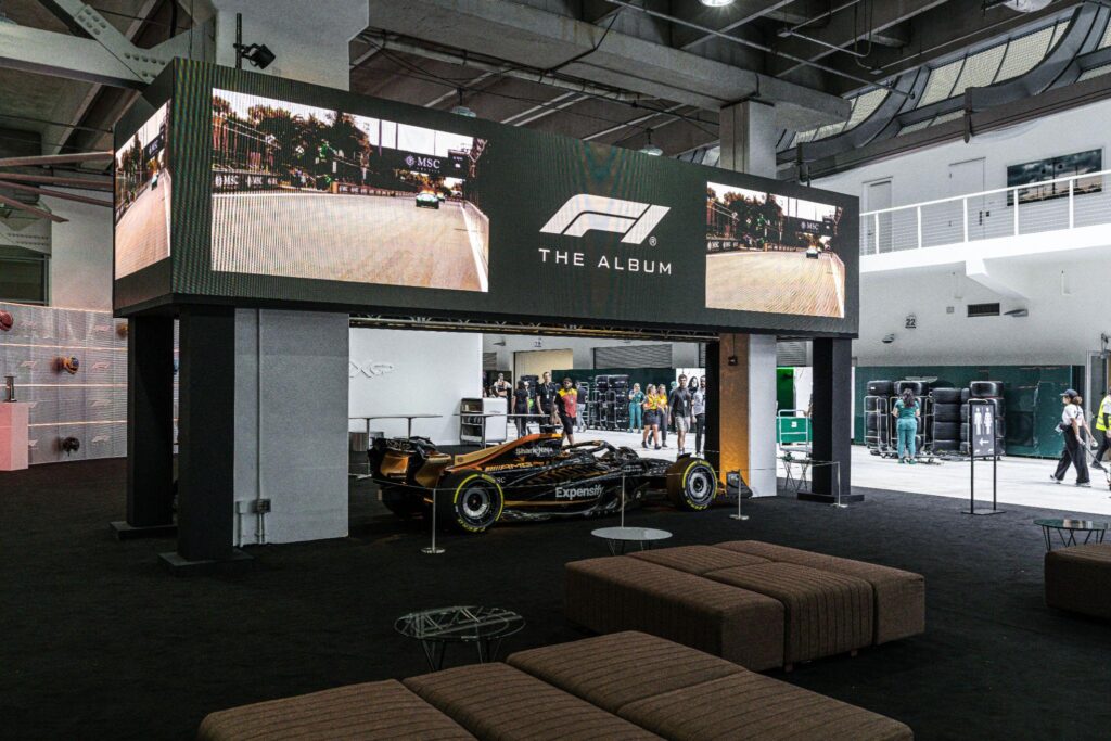 Formula 1 exhibition space featuring F1 The Album branding, large digital display screens and a Formula 1 race car showcased inside an event venue.
