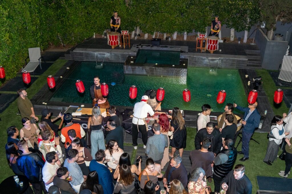 Audience enjoying a Japanese-themed experiential event featuring live cooking, taiko drummers, and lantern decorations around a swimming pool.